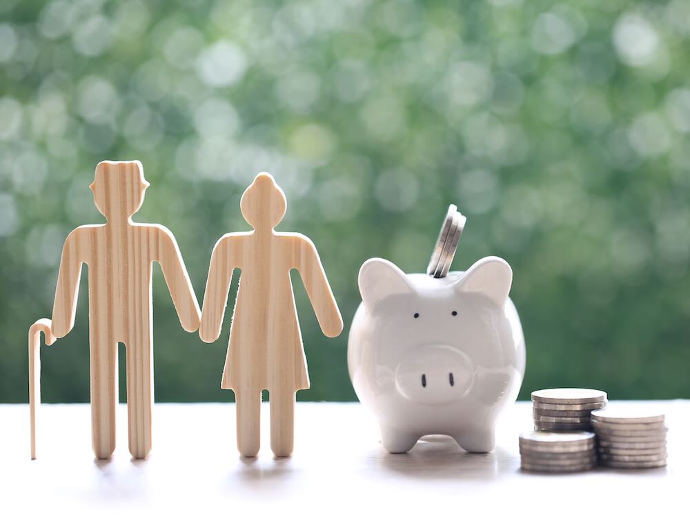 Retirement concept: wooden cutouts of a senior man and woman beside a full piggy bank